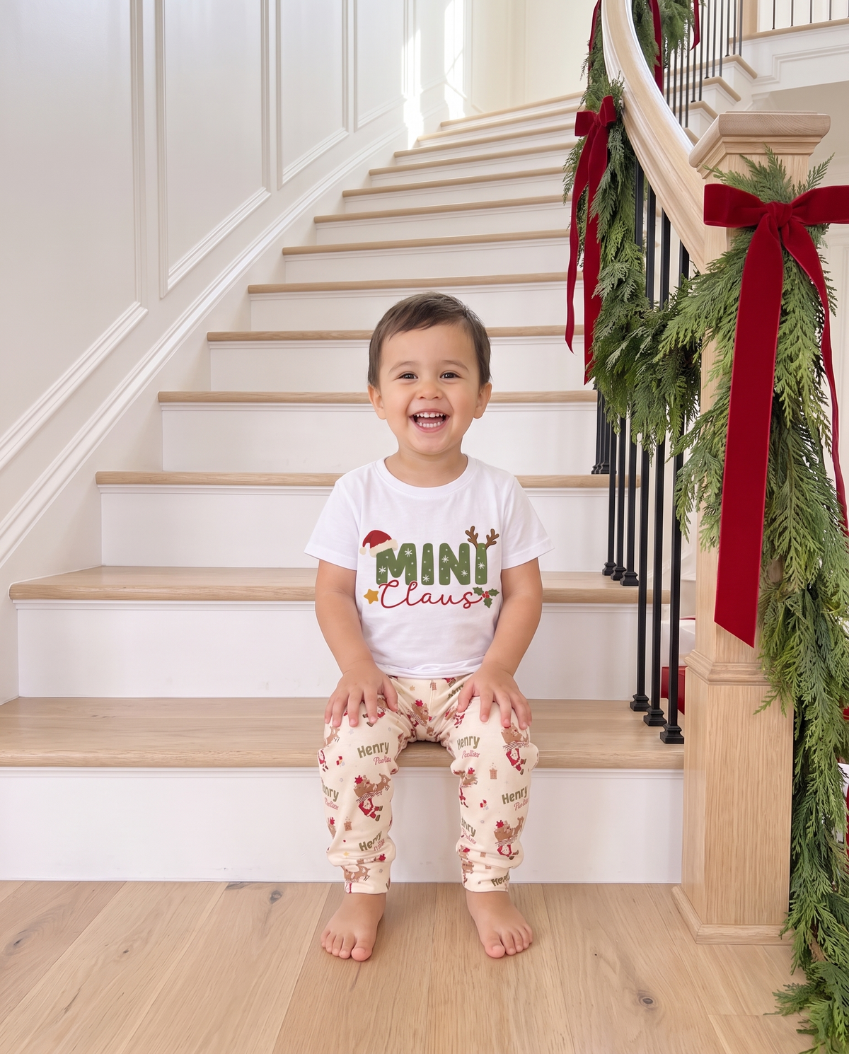 Toddler in the Mini Claus graphic tee and Santa's Joyride pants on the staircase