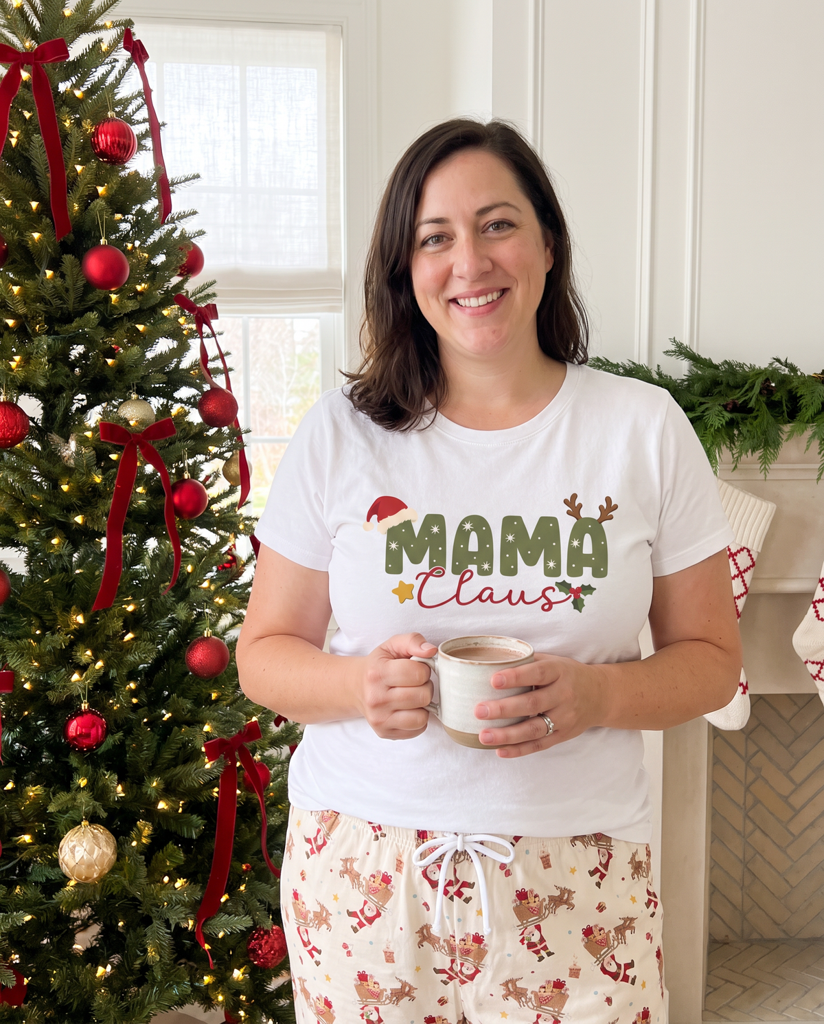 Woman in the Mama Claus graphic tee holding a mug by the Christmas tree