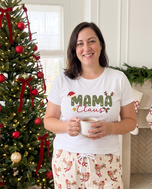 Woman in the Mama Claus graphic tee holding a mug by the Christmas tree